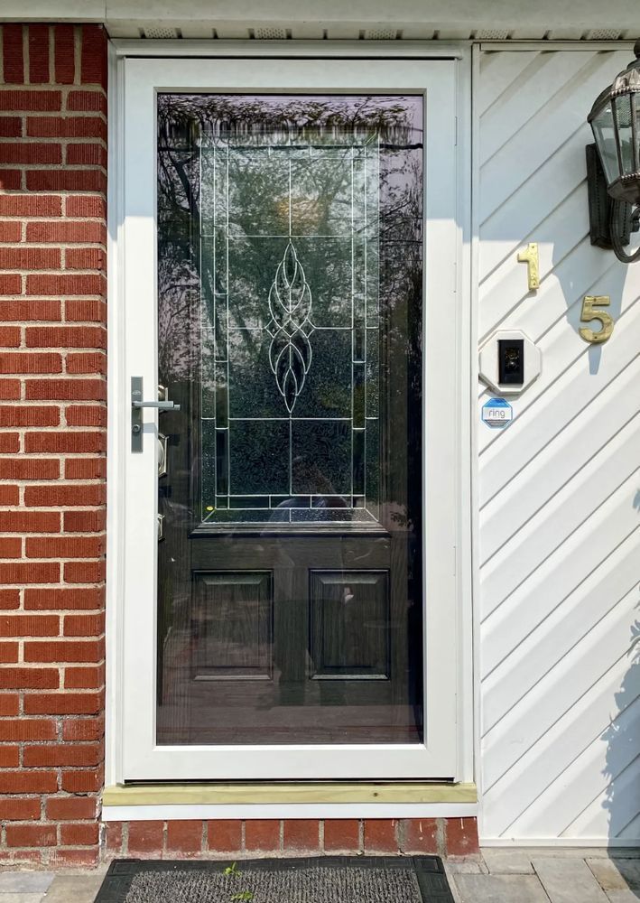 Front door with decorative glass panel, surrounded by white trim, brick and siding. House number
