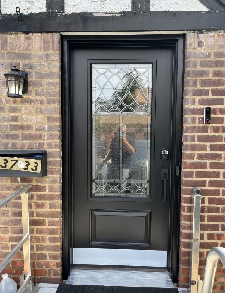 Black front door with glass panel, brick facade. Person reflected in glass.