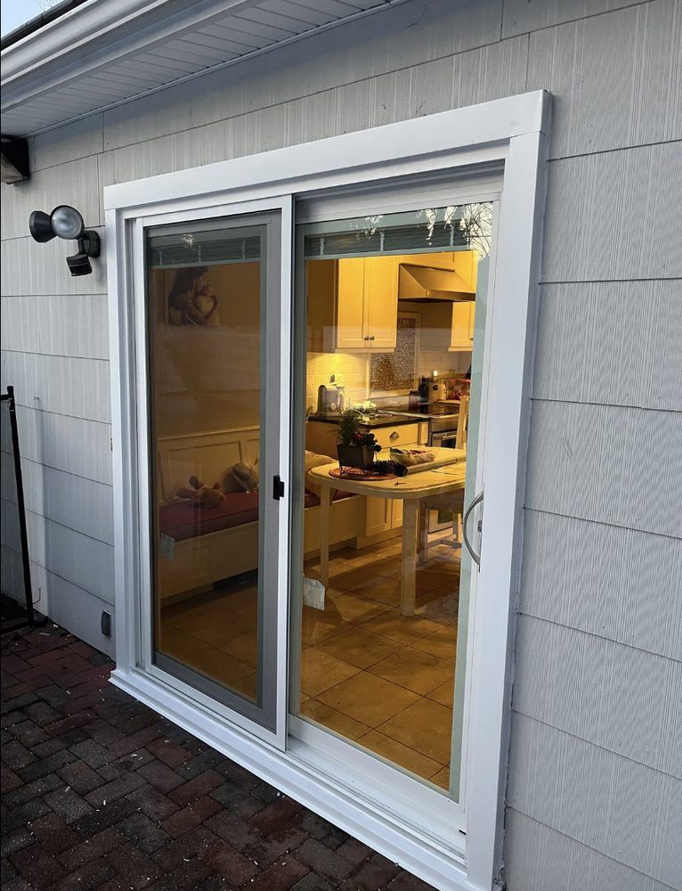 White sliding glass door on a white siding wall, reflecting a kitchen.