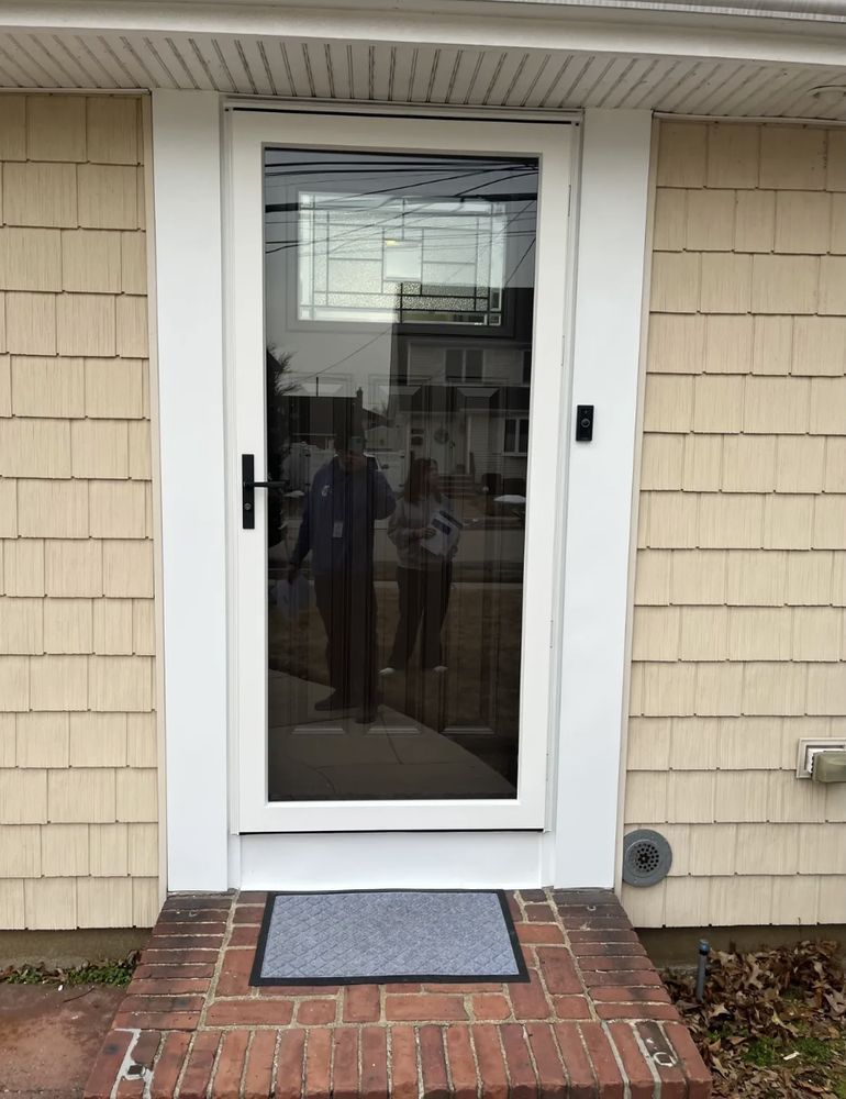 A glass storm door with white trim on a brick stoop with a welcome mat, beige siding.