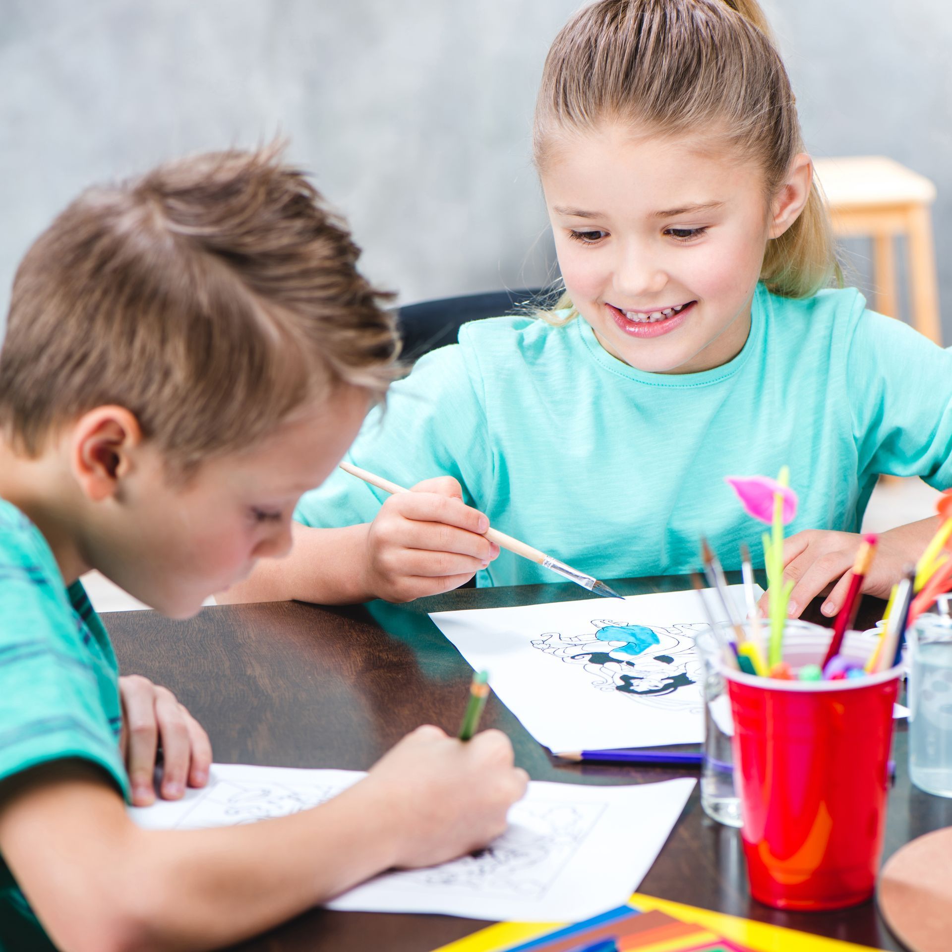 A boy and a girl are sitting at a table painting