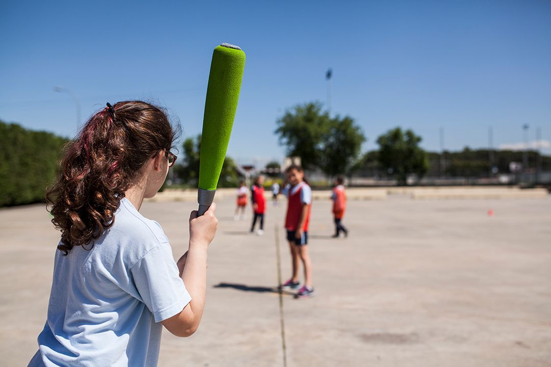A girl is holding a green baseball bat in a field.