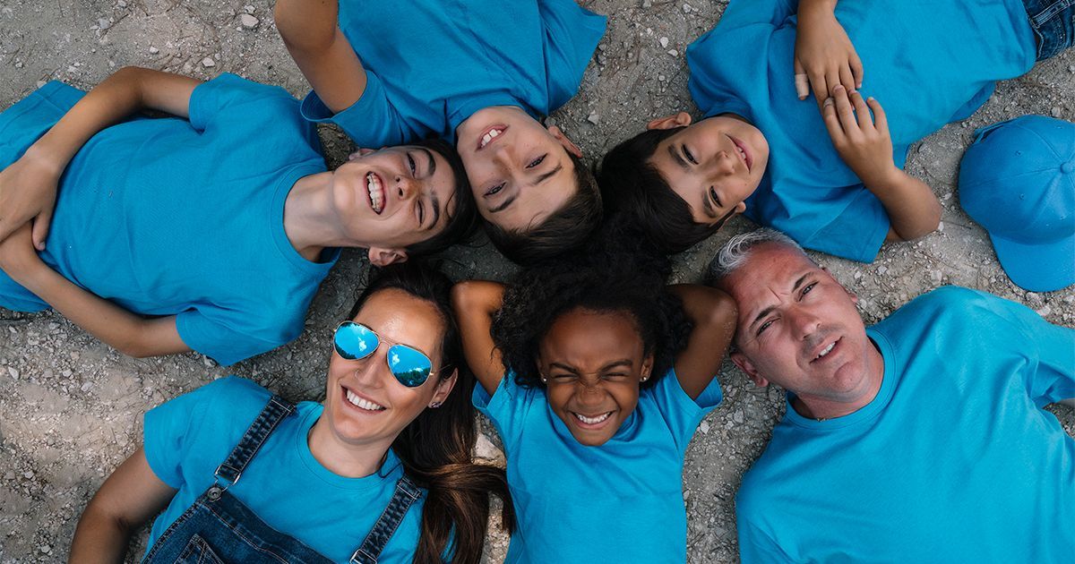 A group of people in blue shirts are laying in a circle on the ground.
