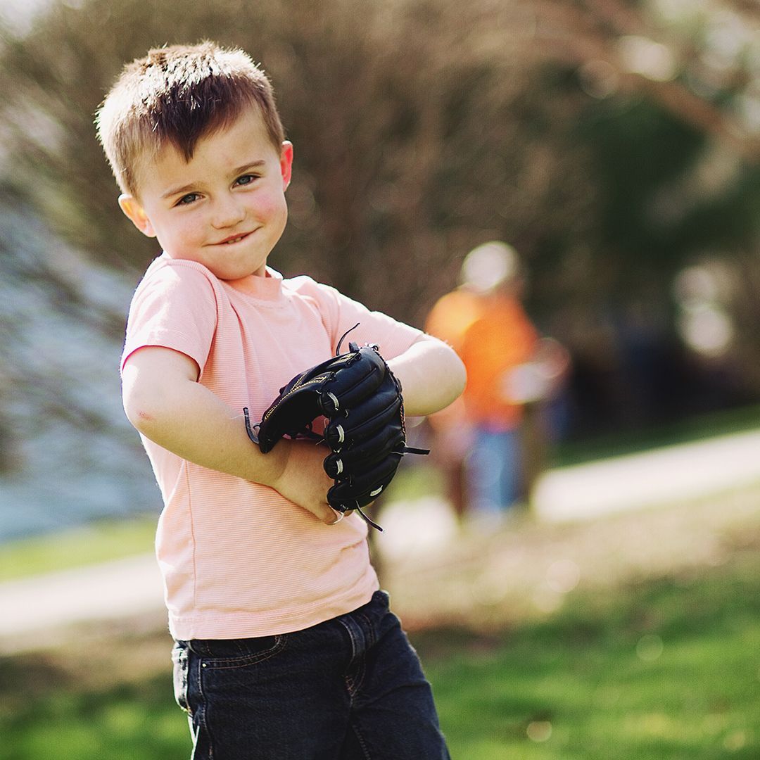 A young boy in a pink shirt is holding a baseball glove