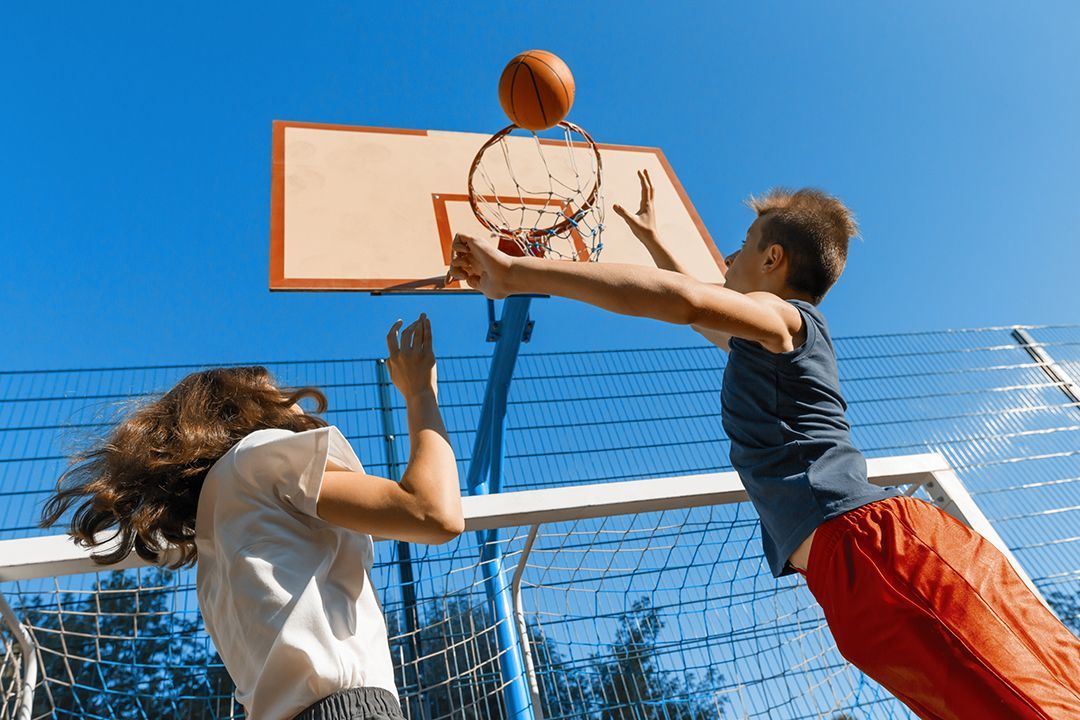 A boy and a girl are playing basketball on a court.