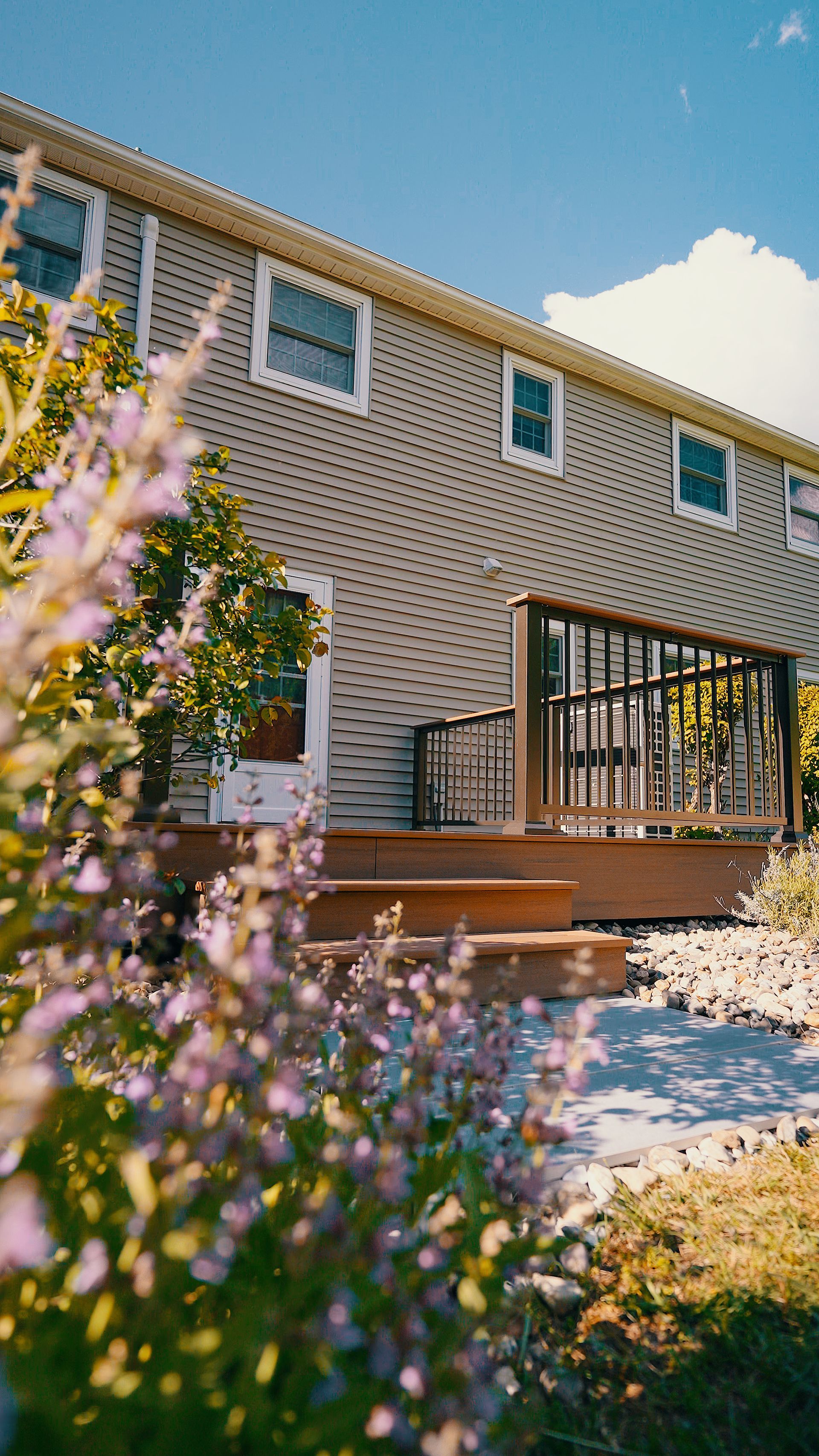 A house with a deck and flowers in front of it.