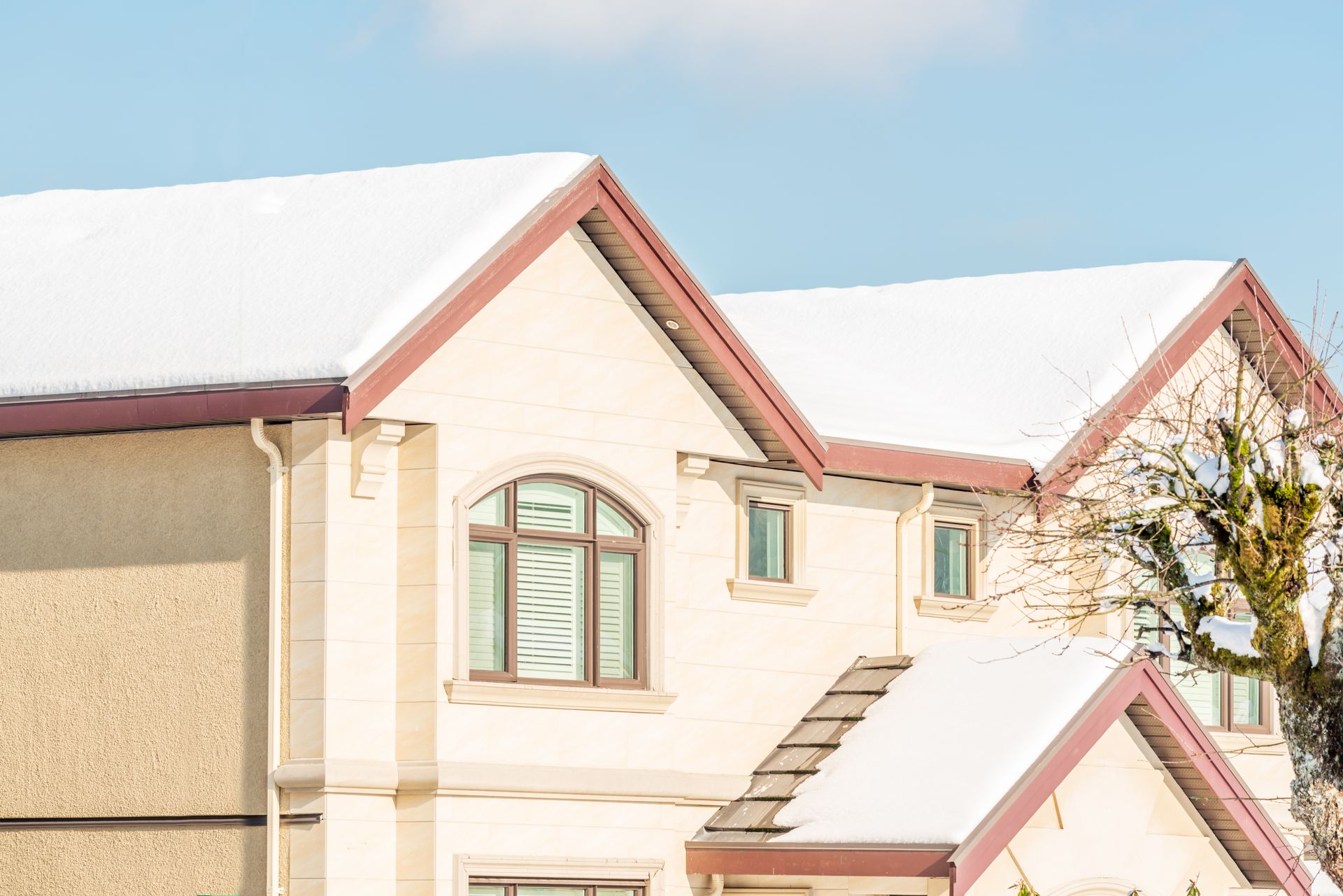 Snow-covered roofs of a cream-colored house with brown trim against a blue sky.