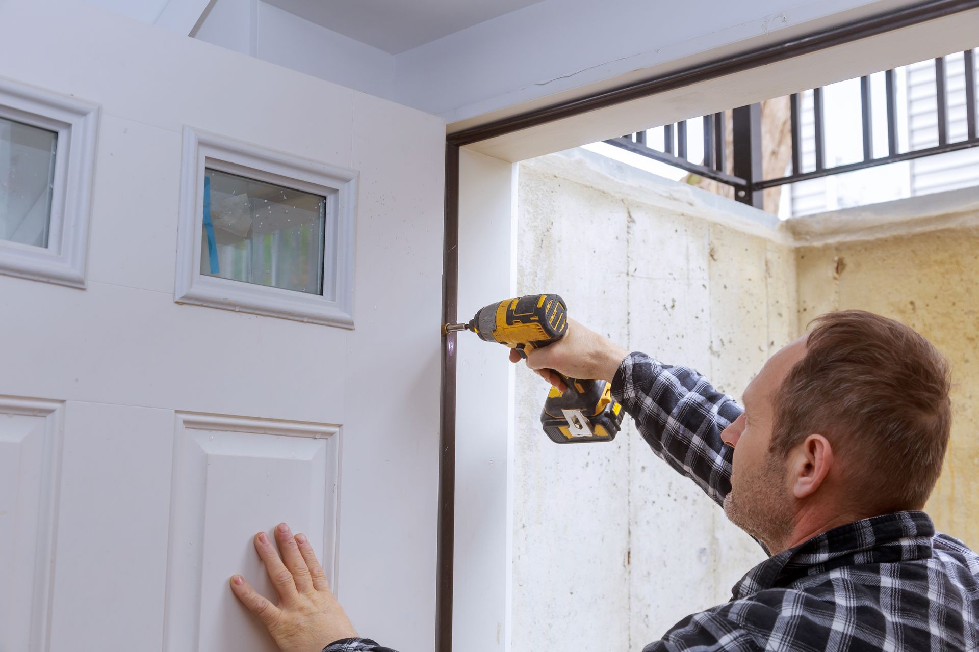 Person installing a white door, using a power drill.