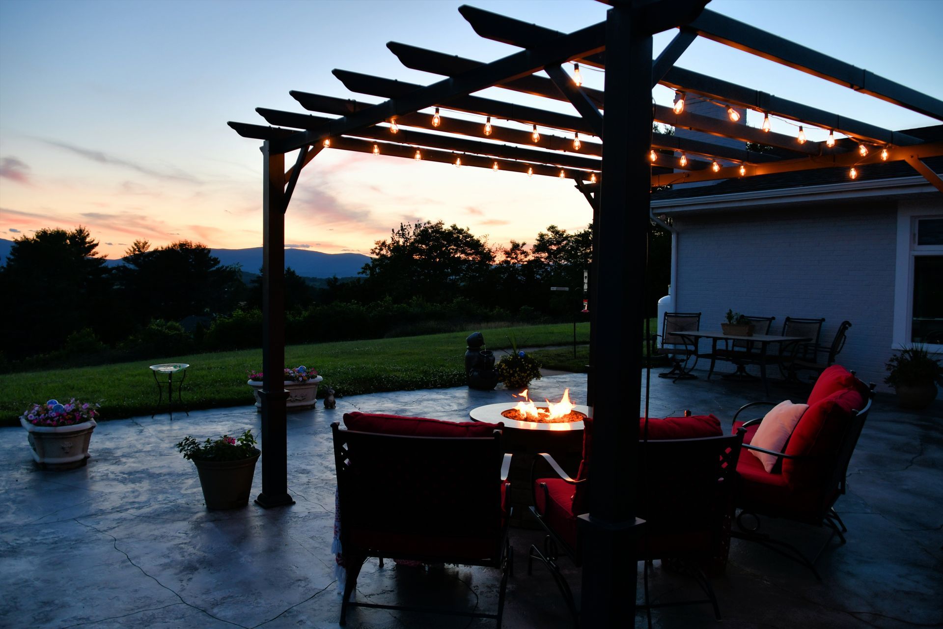 A patio with a fire pit under a pergola at night