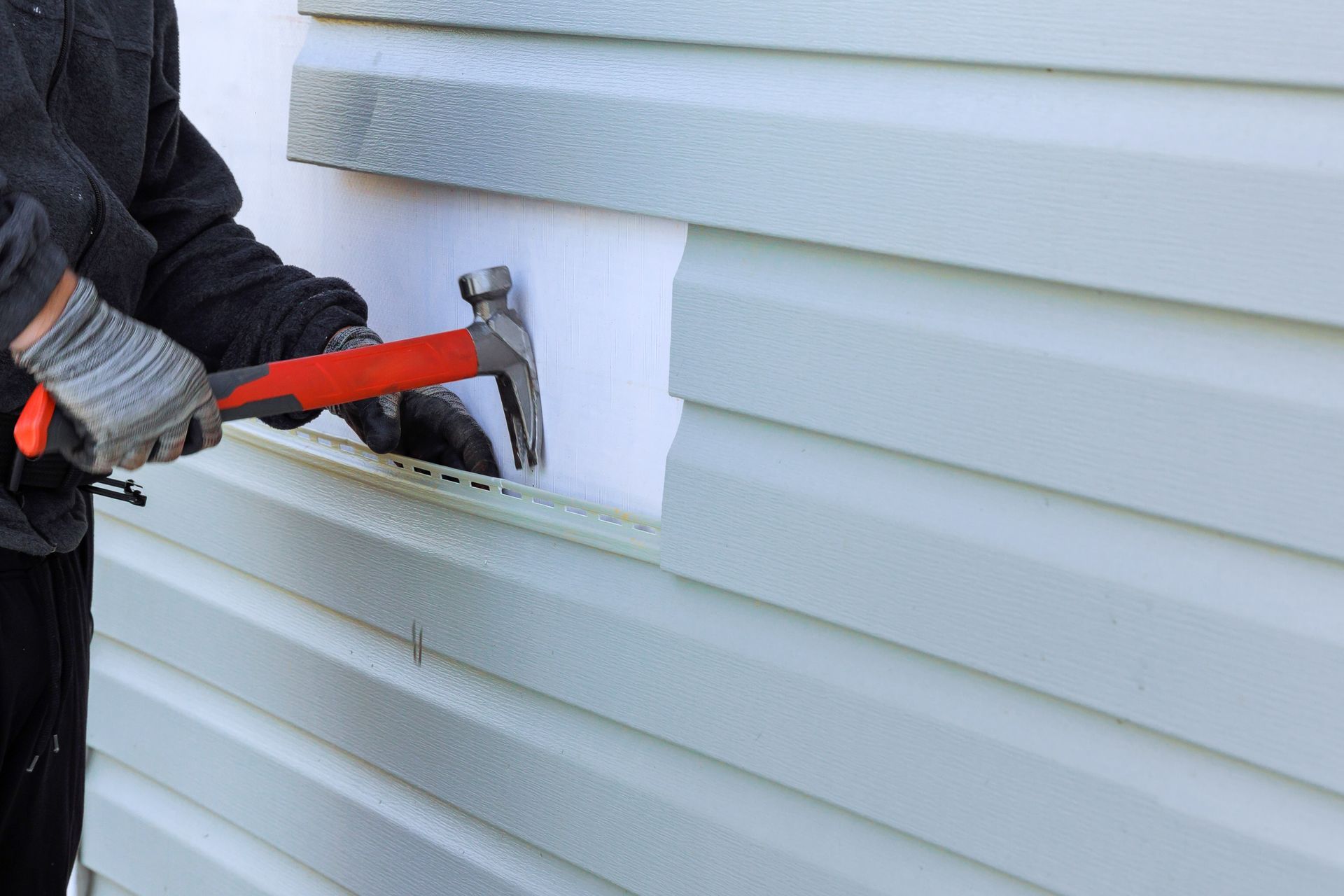 Person hammering nails into white siding on a house exterior