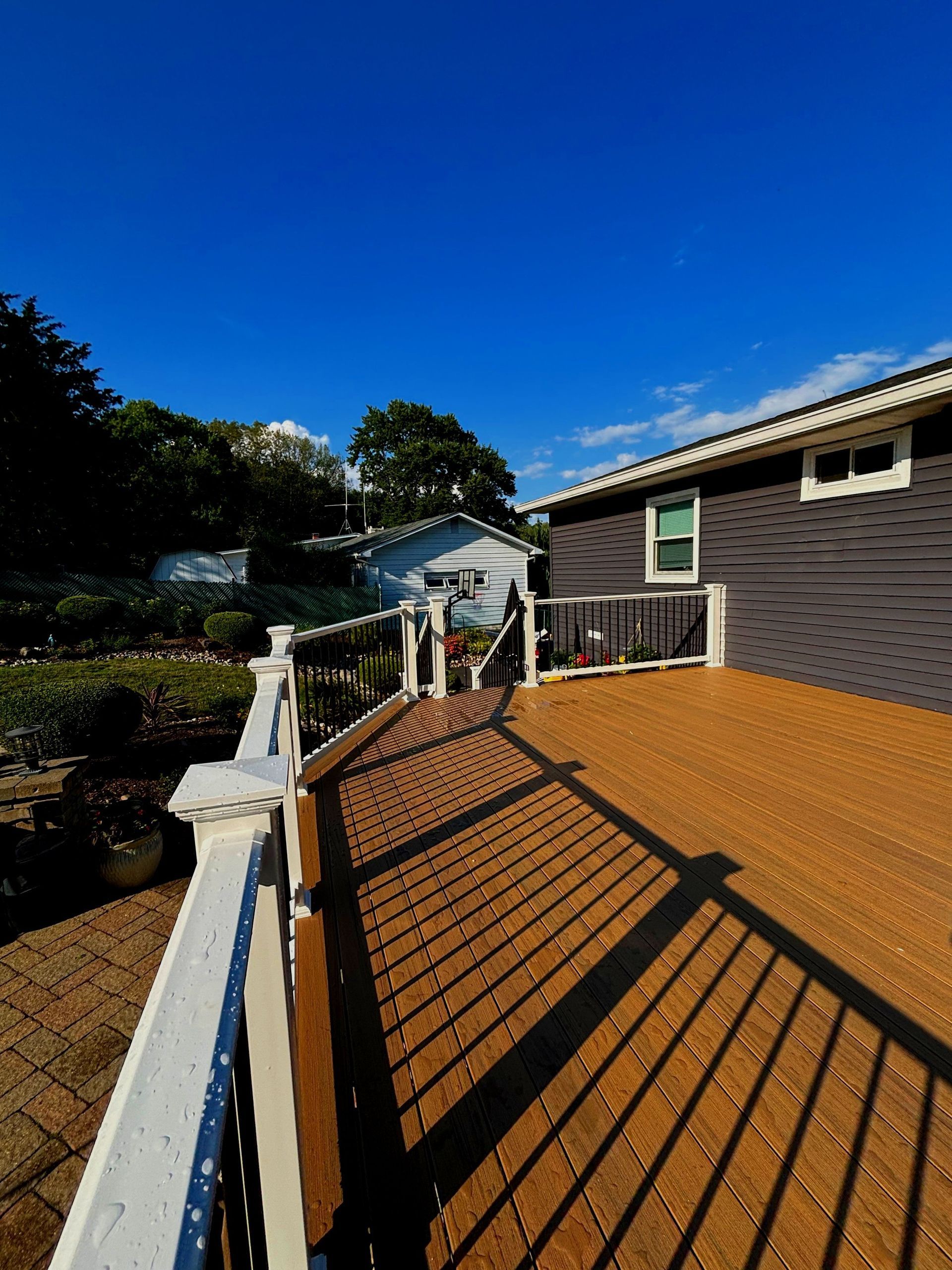 A deck with a white railing and a house in the background