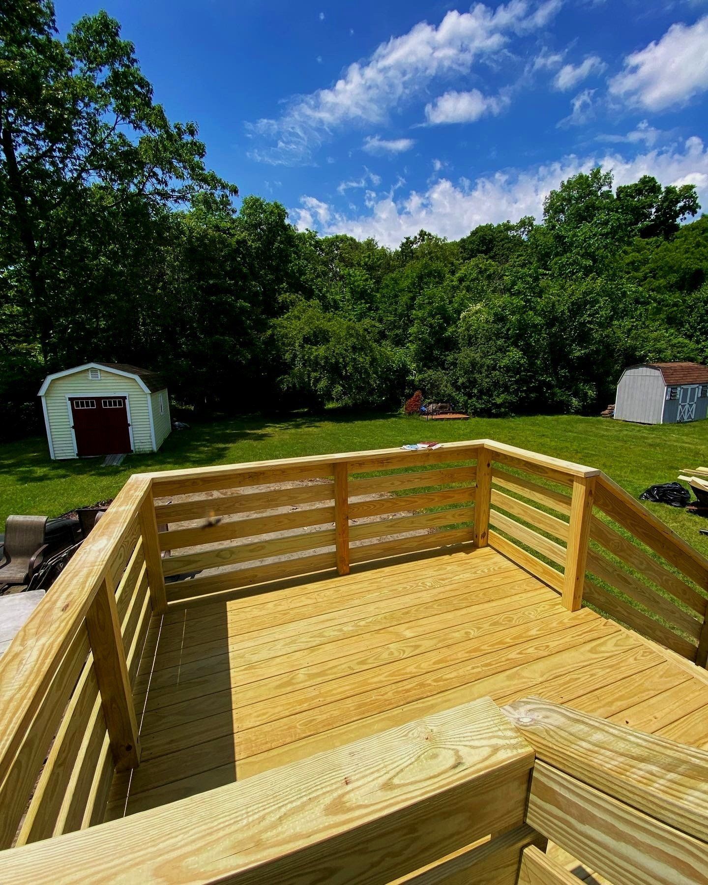 A wooden deck with stairs leading up to it and a shed in the background.