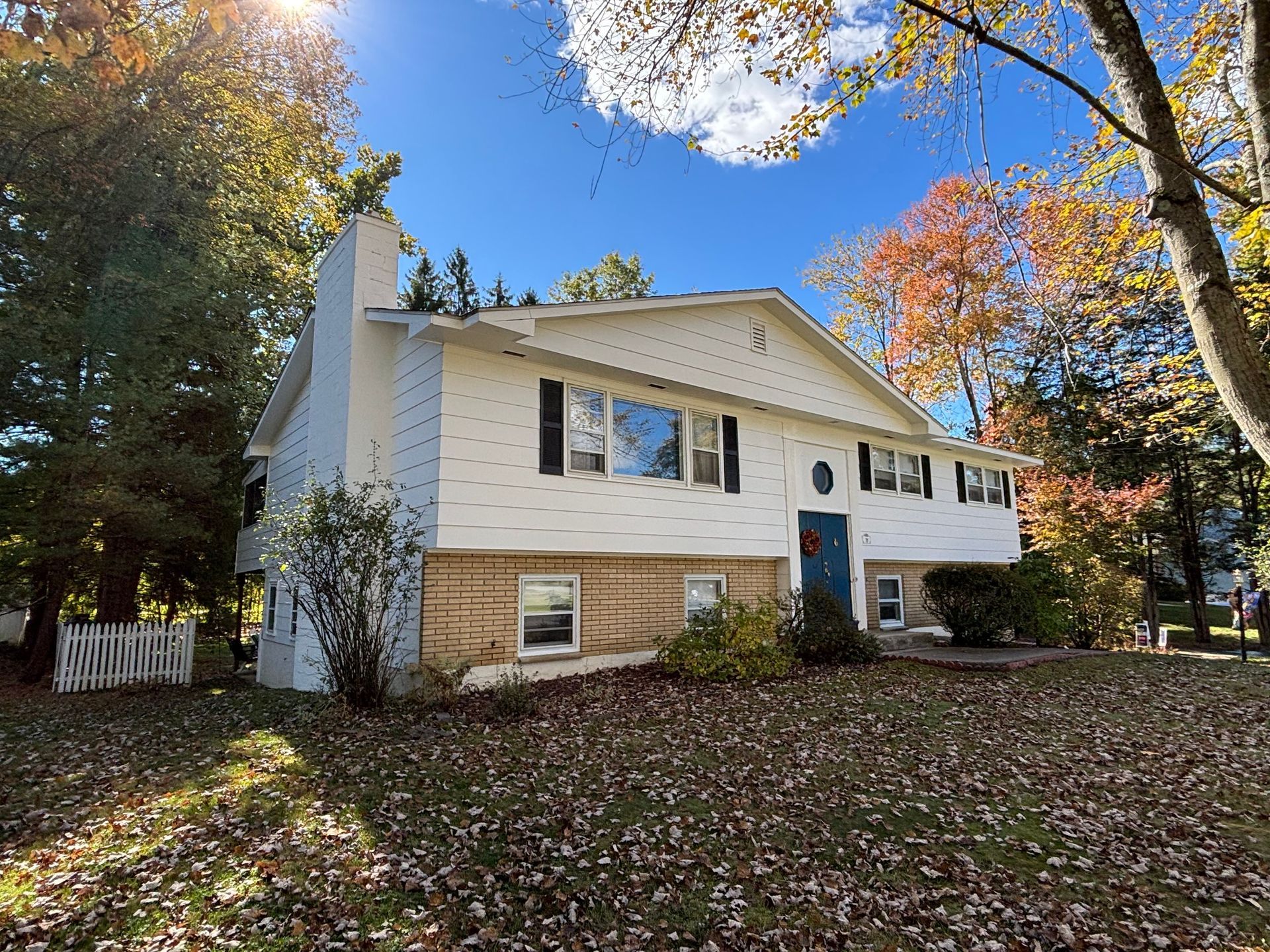 A white house with a blue door is surrounded by trees and leaves
