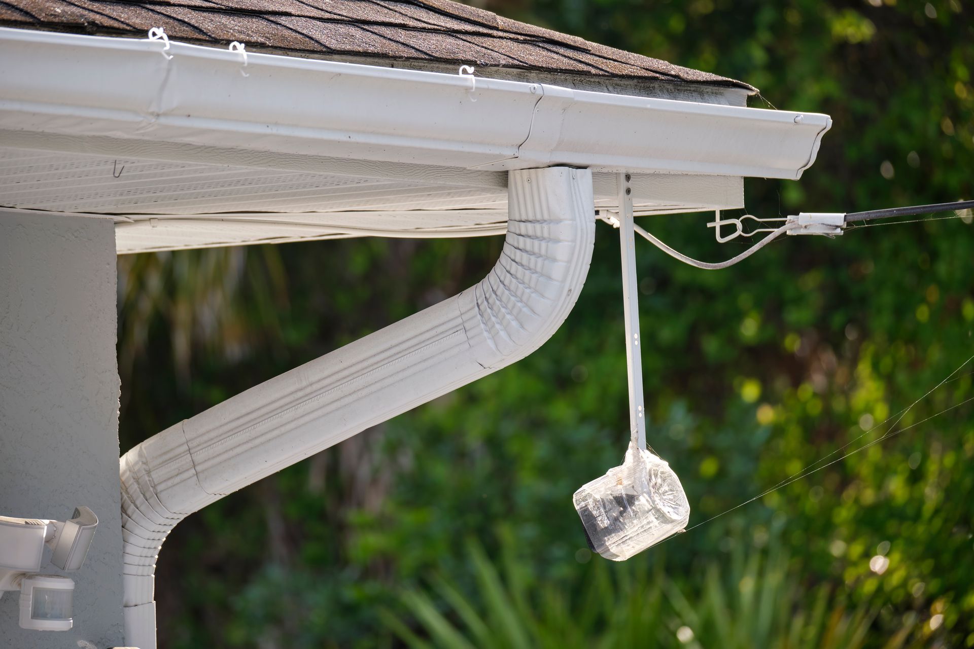 White gutter and downspout on a house roof with a small object hanging from the gutter