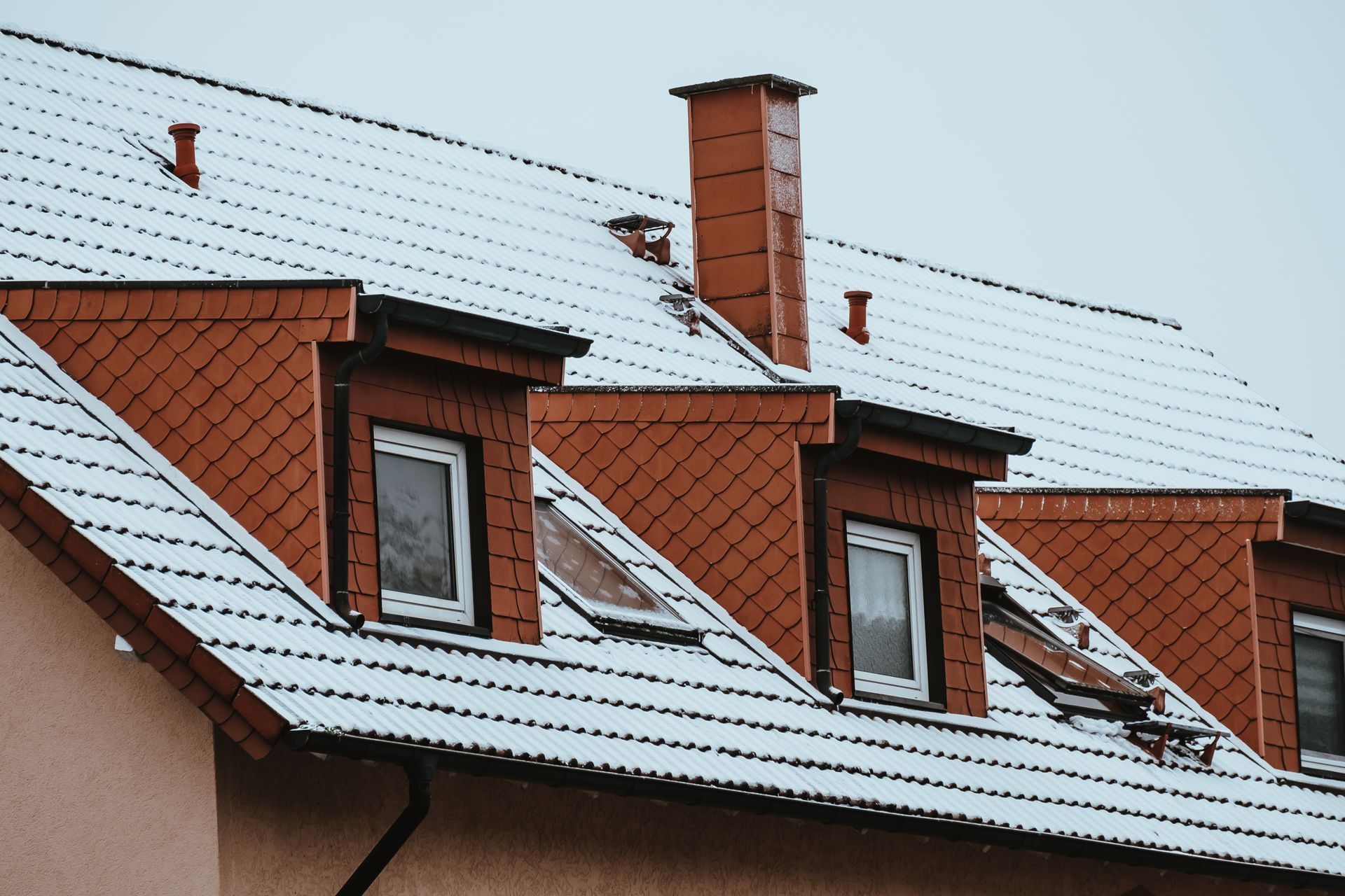 Snow-covered red roof with dormer windows and a chimney