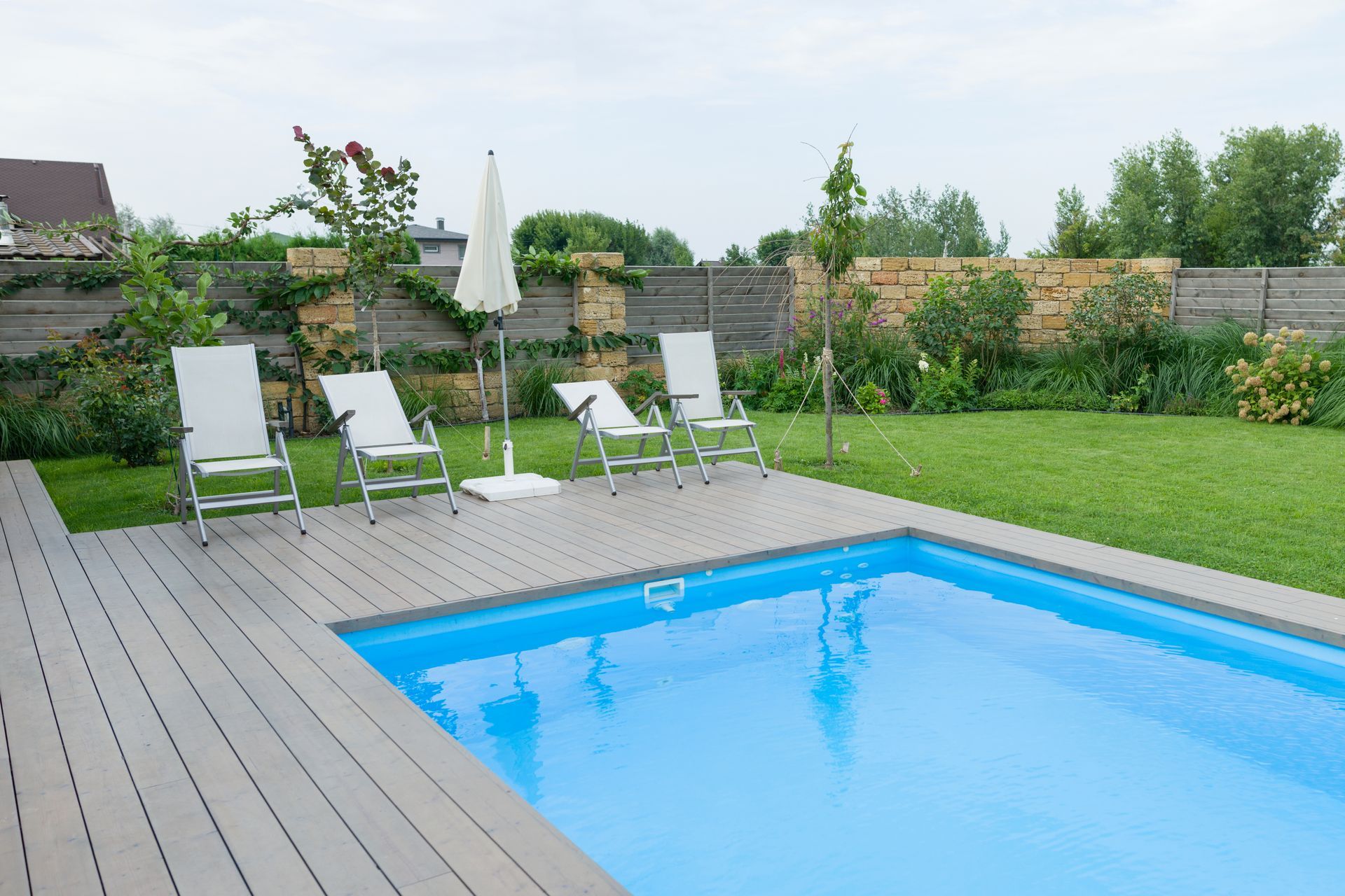 There is a large swimming pool in the backyard with chairs and umbrellas.