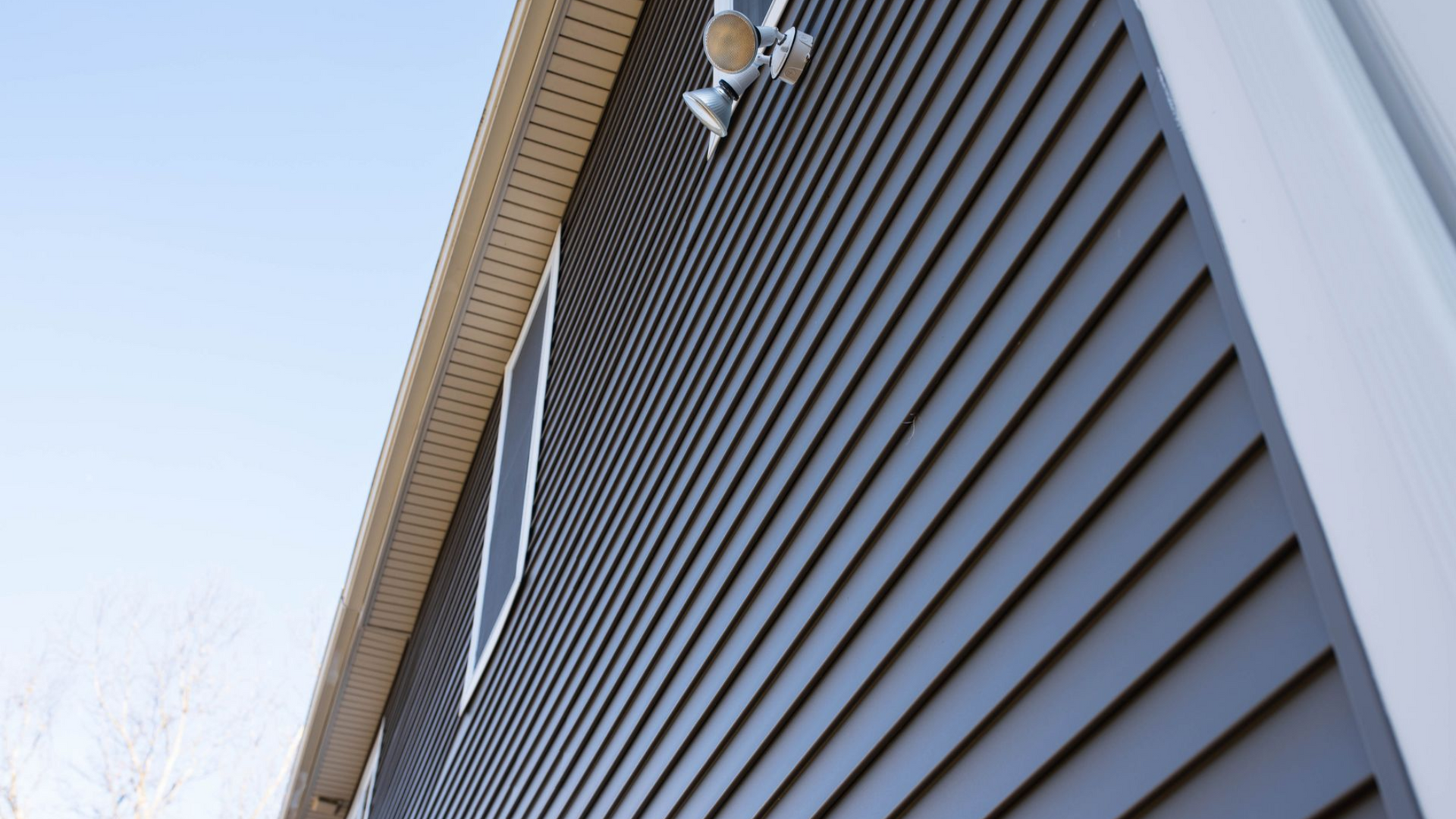 Dark gray siding on a building with white trim, tan eaves, and security lights.