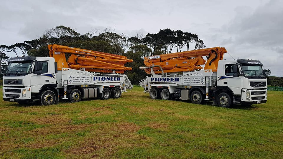 Two concrete pump trucks are parked in a grassy field.