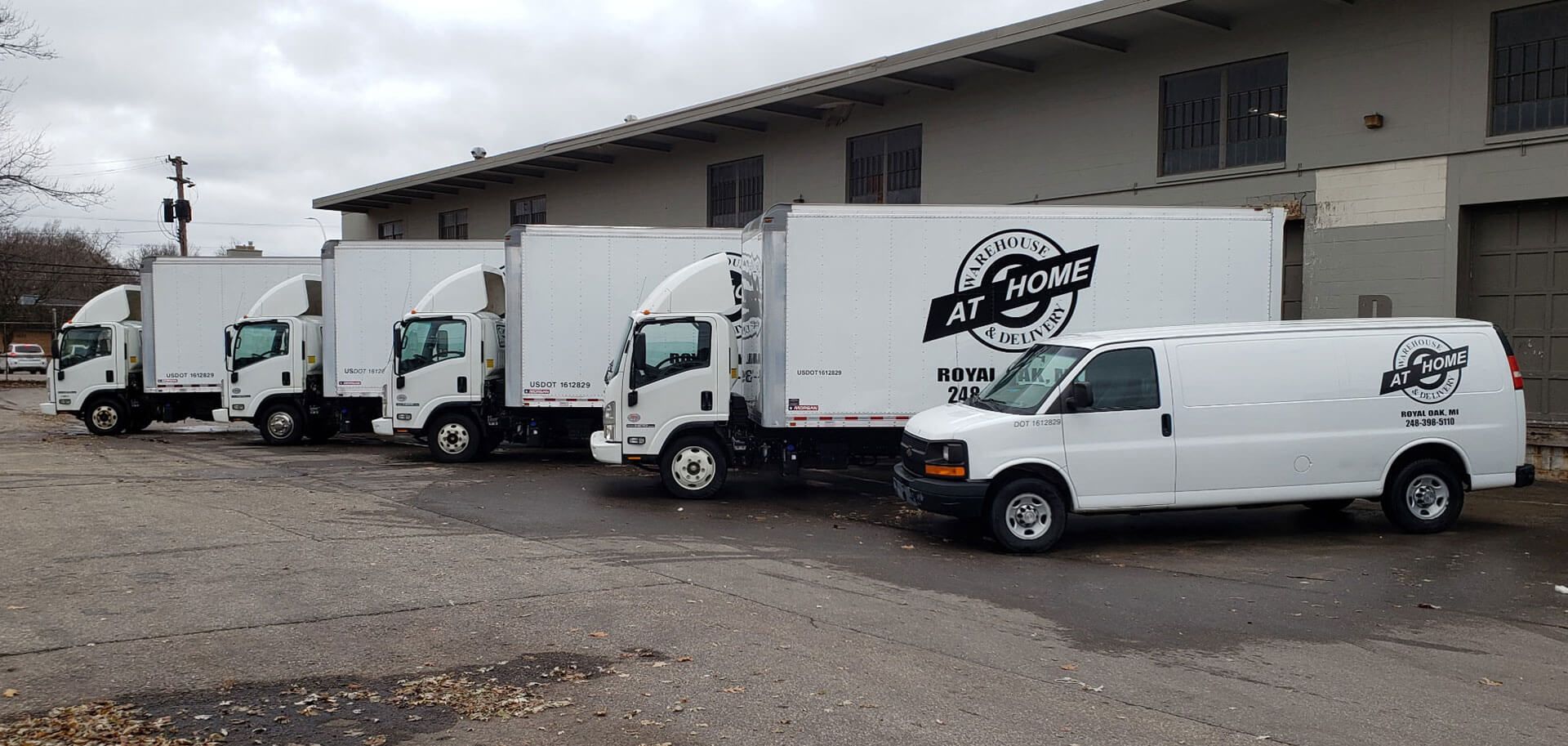 Several white moving trucks and a van parked in front of a building on a cloudy day.