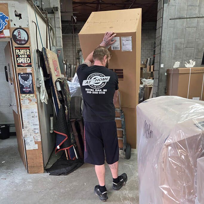 Man moving large cardboard box on a dolly in a warehouse setting.