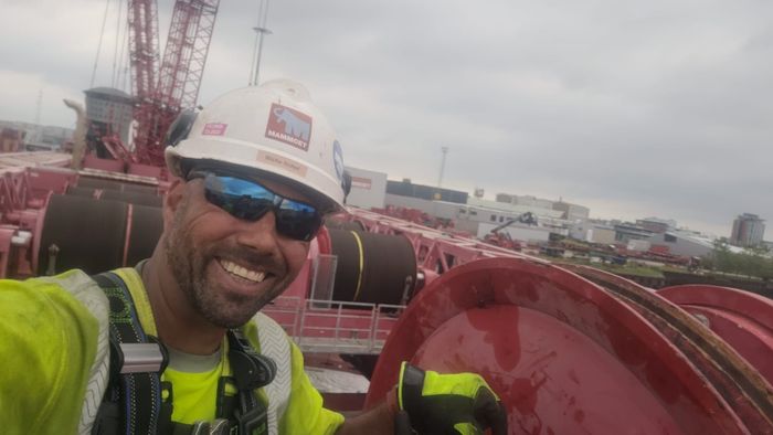 A man wearing a hard hat and sunglasses is taking a selfie.