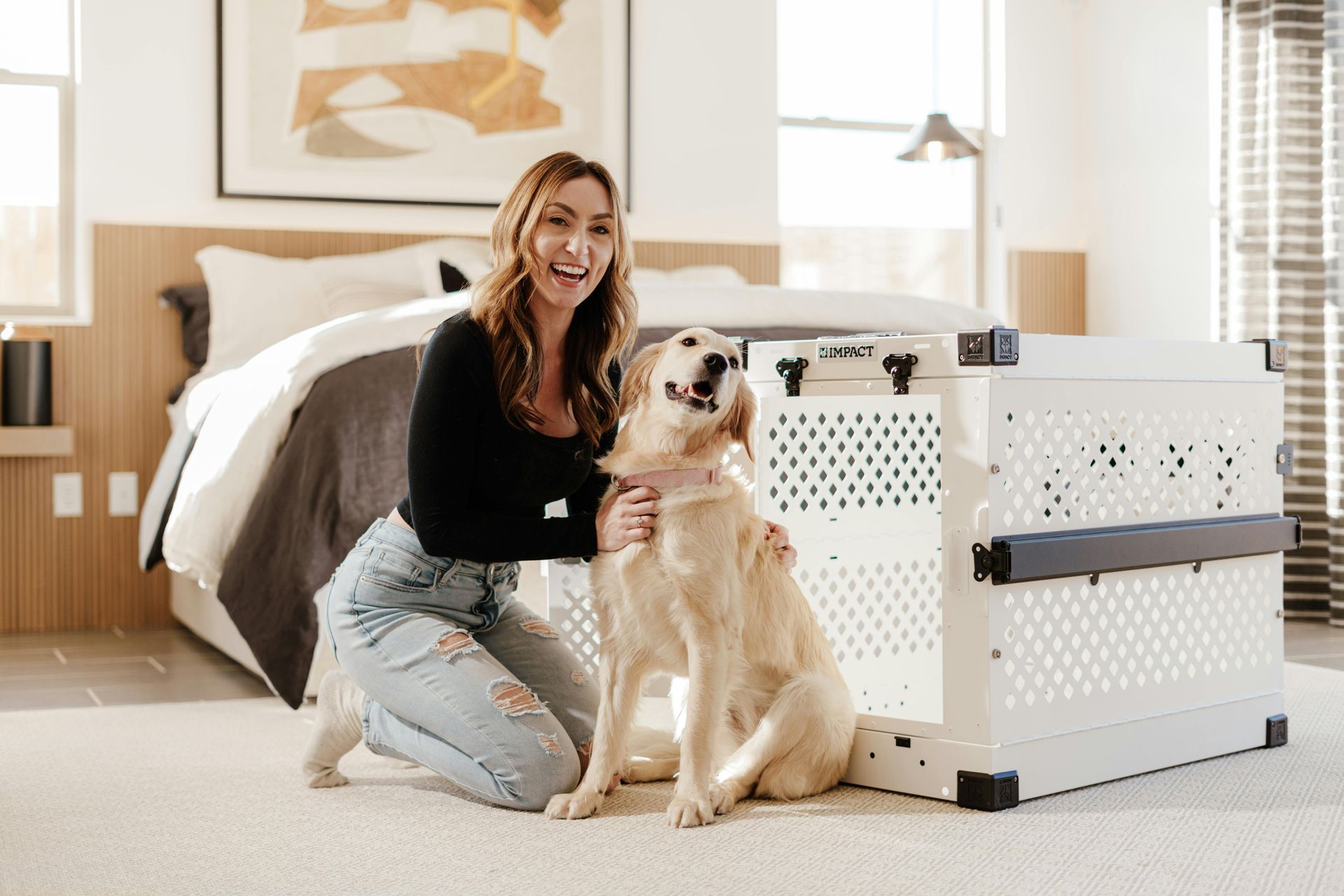 A woman is kneeling down next to a dog in a room with a dog crate.