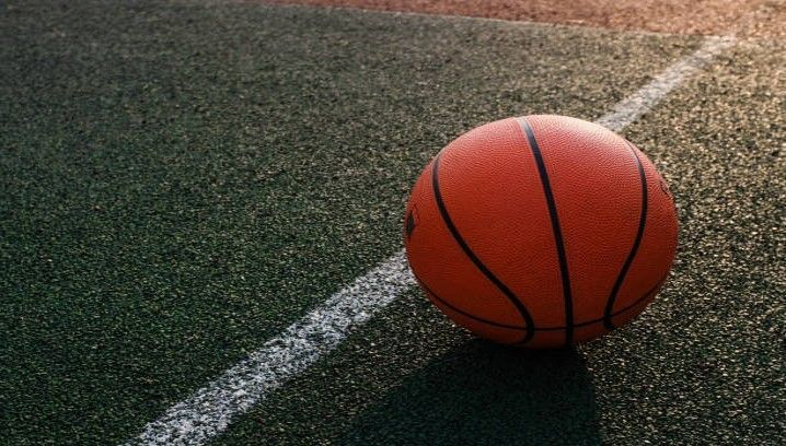 Basketball on a green court, near a white line, with sunlight.