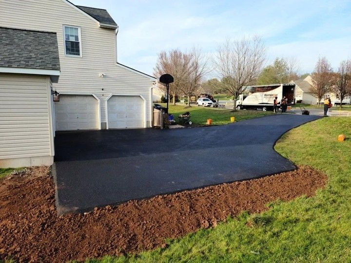 Newly paved asphalt driveway next to a beige house with a garage; workers near the road.