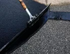 Applying black sealant to asphalt with a squeegee