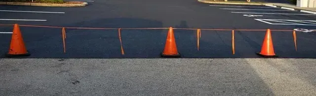 Orange traffic cones connected by orange tape block access to parking spaces