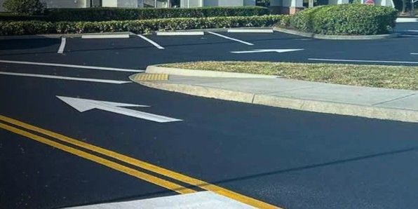 Paved road with white directional arrows, yellow lines, and a curb leading into a parking area