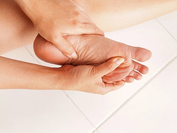 Woman holding her painful foot, showing common condition treated by a foot doctor.