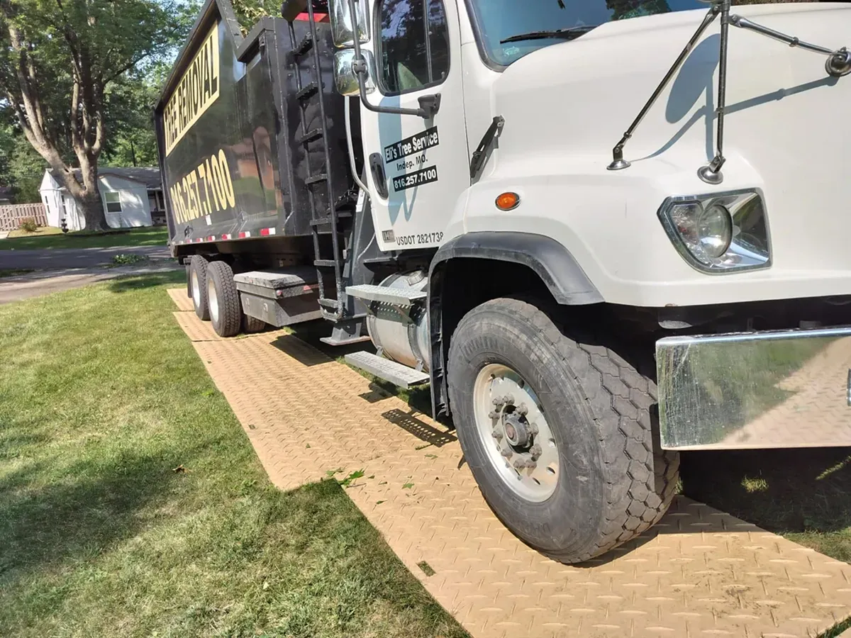 A large white dump truck parked on temporary protective floor mats laid across a green lawn.