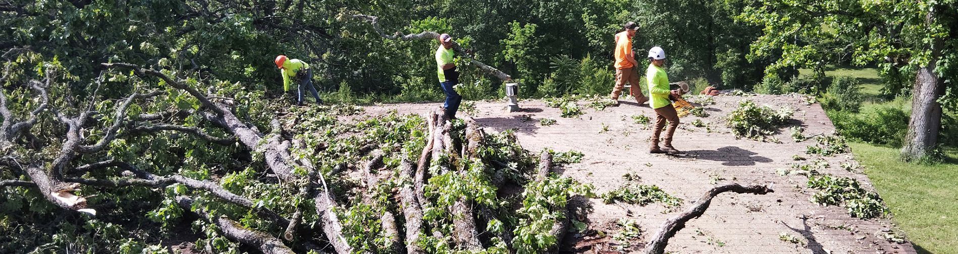 Workers in safety vests and hard hats clearing debris from a damaged roof after a storm.