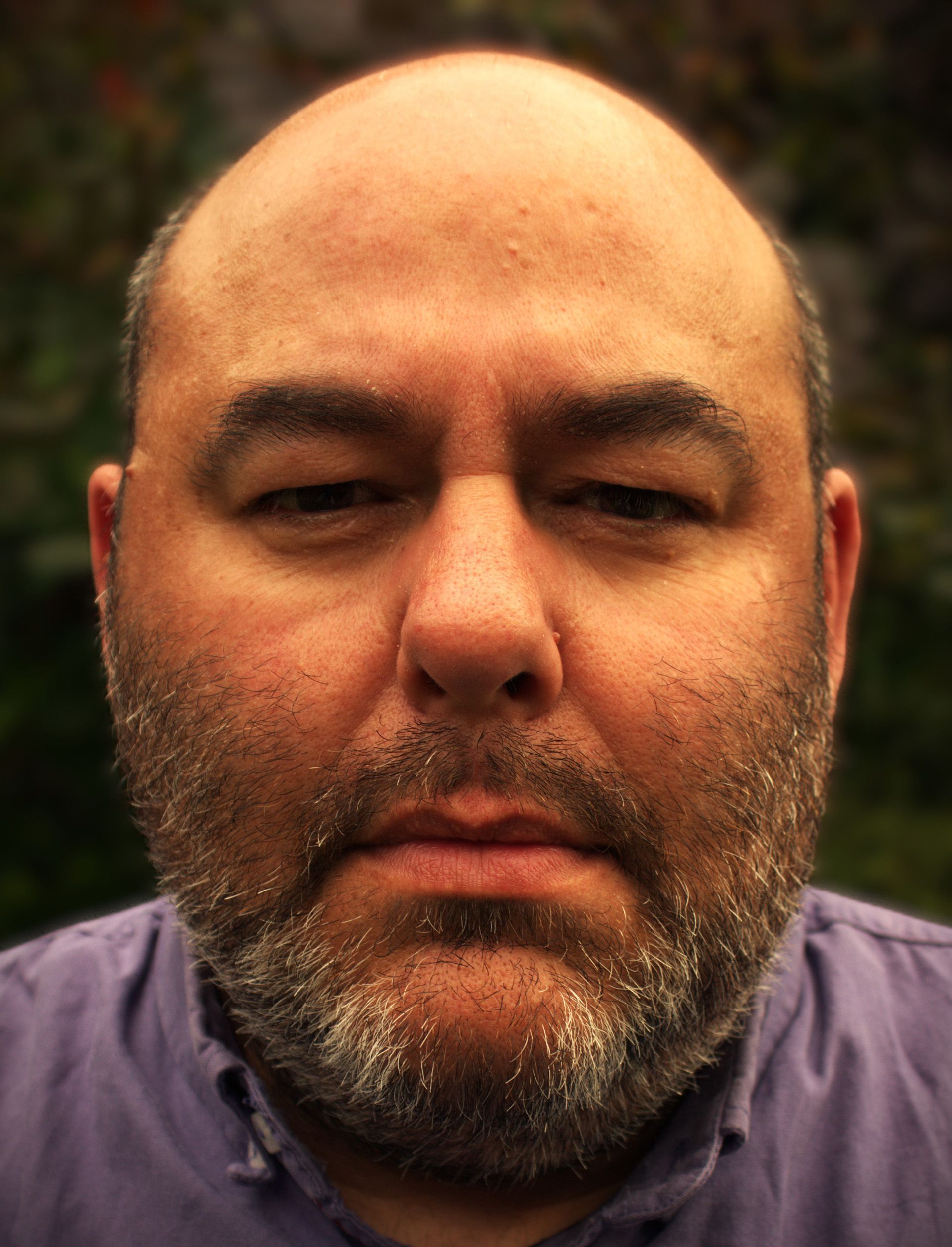 A bald man with a beard and a purple shirt is looking at the camera.