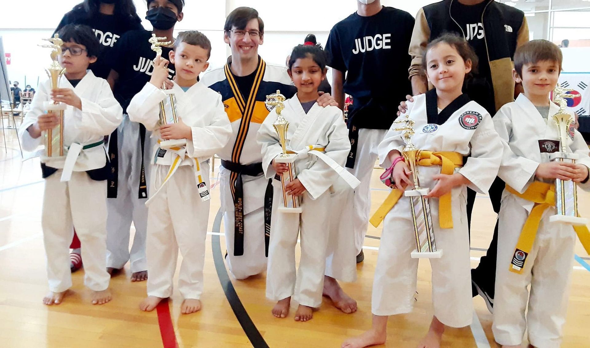 a group of children in karate uniforms are posing for a picture while holding trophies .