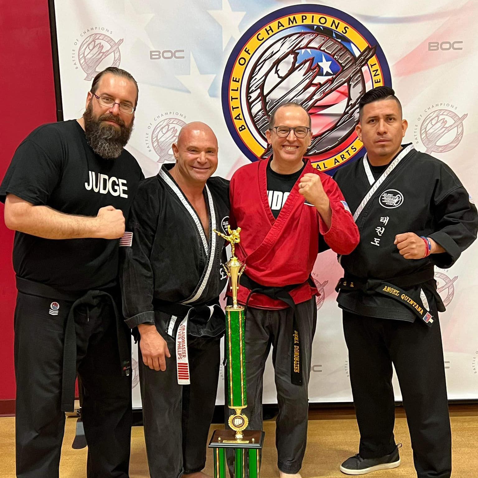 a group of men in karate uniforms are posing for a picture with a trophy .