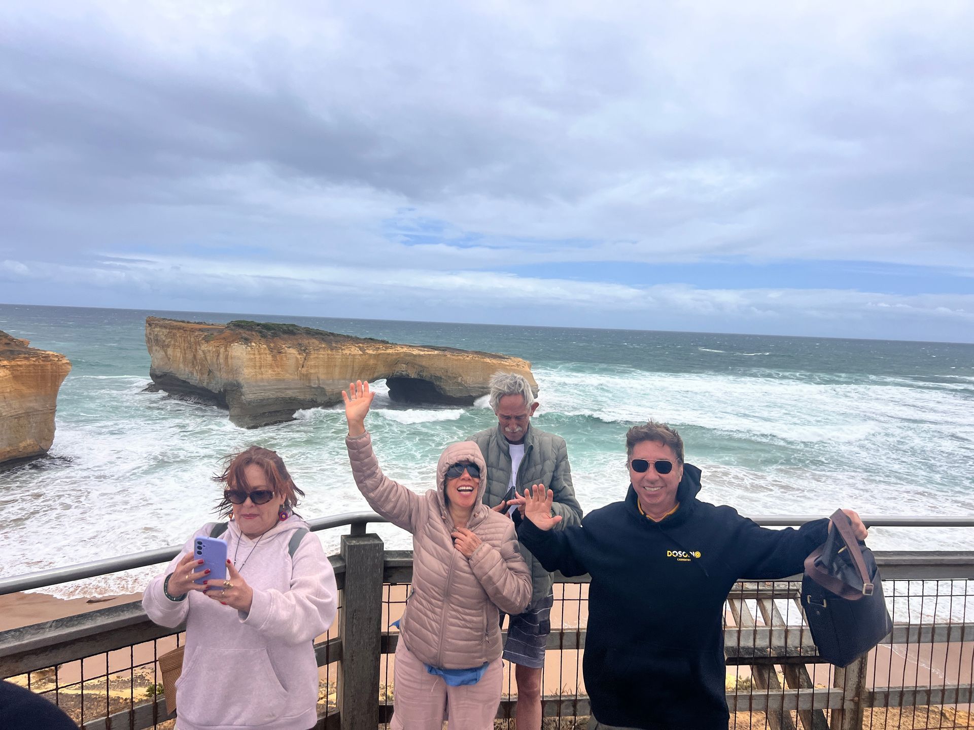 Urubu-de-cabeça-vermelha com asas estendidas sobrevoando um litoral rochoso e o oceano.