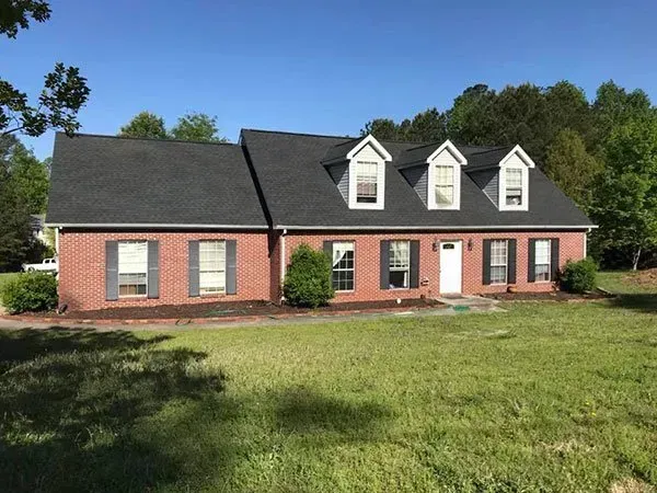 A one-story brick house with a dark shingled roof, three dormer windows, and a front lawn under a clear blue sky.