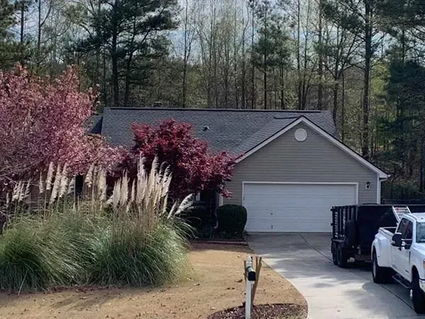 A suburban home with a gray roof and siding, featuring a driveway with a truck, a dumpster, and flowering landscaping.