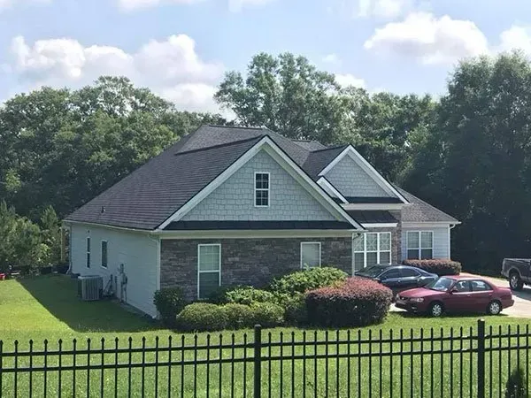 A single-story suburban house with stone and light-colored siding, a dark roof, and two cars parked in the driveway.