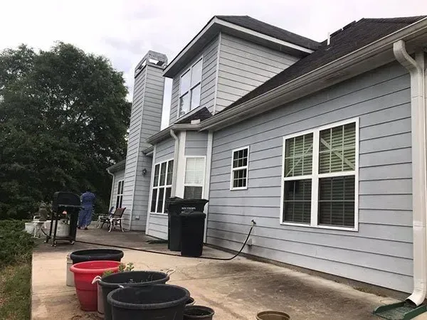 Light blue house exterior with a chimney, patio, and several dark planters in the foreground.