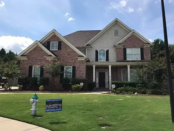 A two-story brick and siding house with a green lawn, a fire hydrant, and a small sign in the front yard.