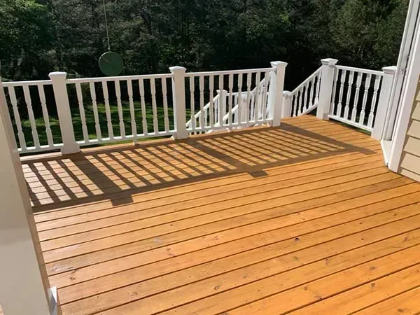 A freshly stained, light brown wooden deck with white railings, looking out over a green yard.