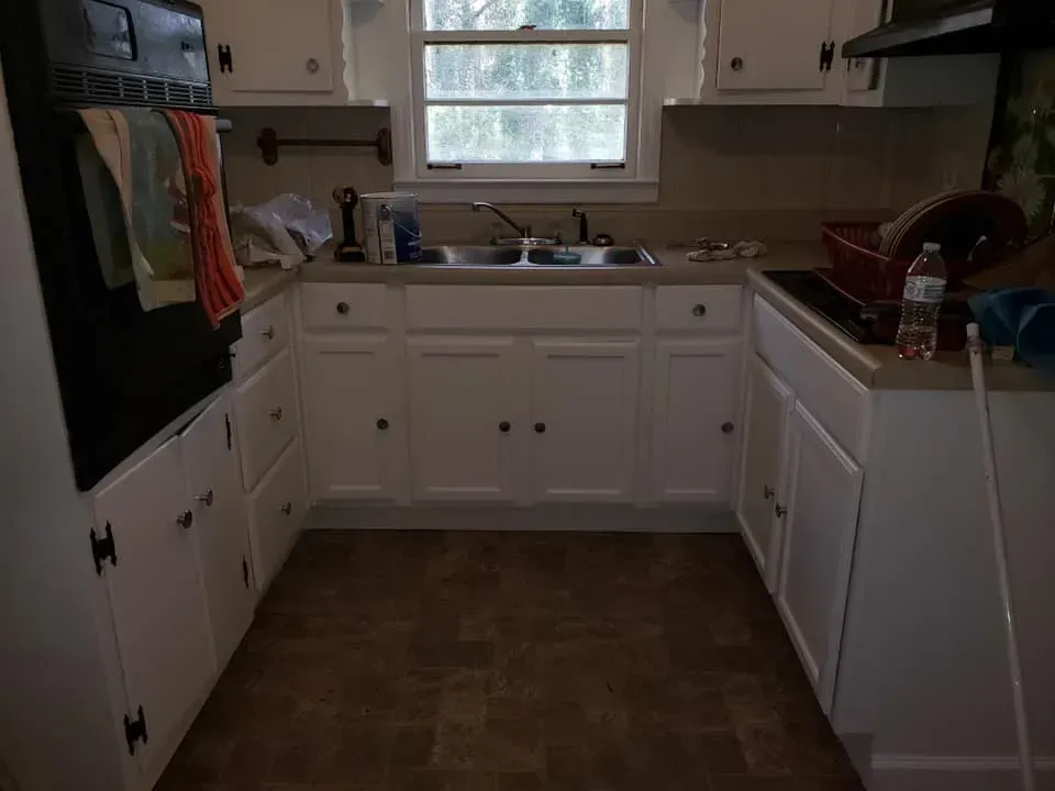 A U-shaped kitchen with white cabinets, a window above a stainless steel sink, and dark brown tiled floors.