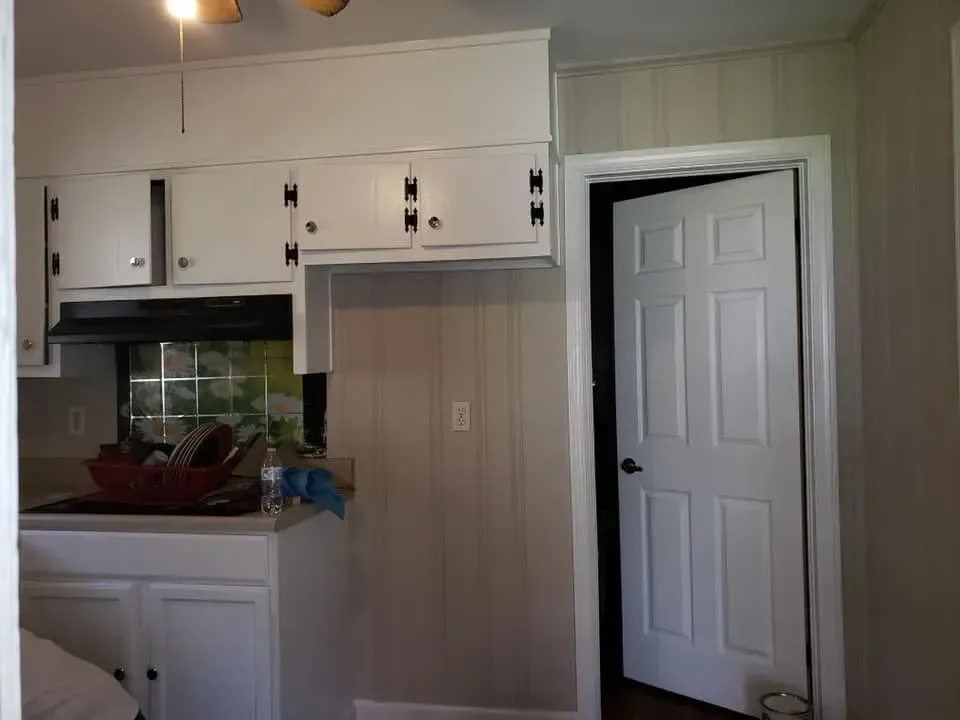 A kitchen area with white cabinets, a black range hood over a sink, and a white six-panel door leading to another room.