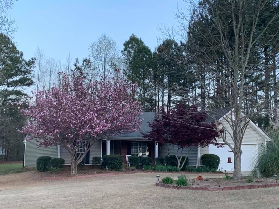 A single-story house with a white garage, surrounded by a blooming pink dogwood and a dark red maple tree.