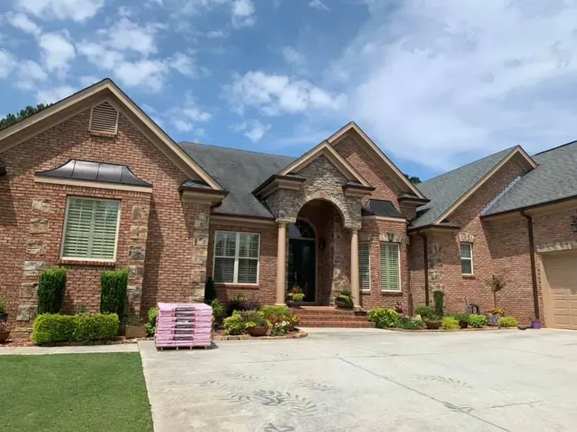 A one-story brick house with a stone entryway, arched front door, and gray roof under a blue, cloudy sky.