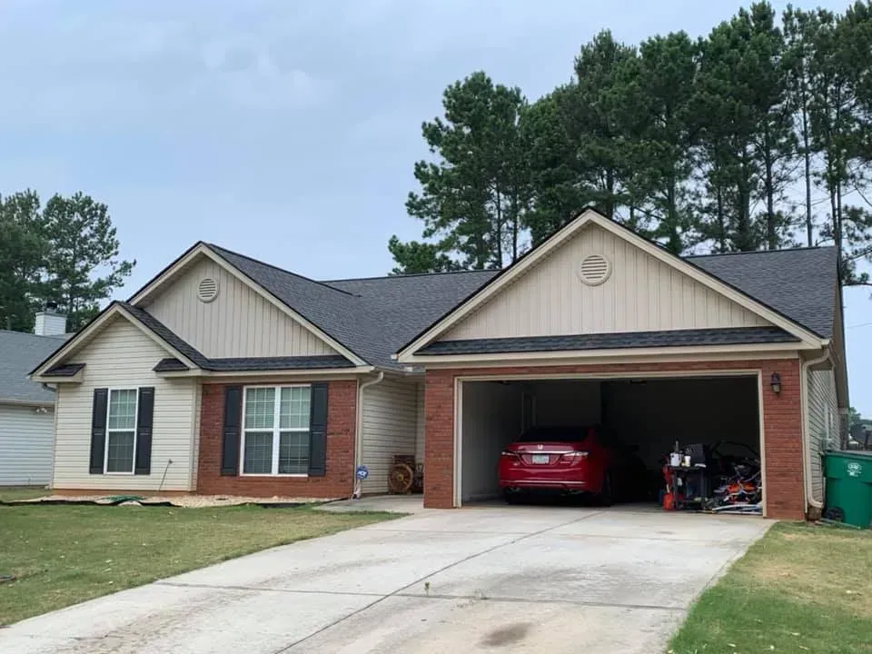 A one-story suburban home with beige siding, brick accents, a gray roof, two windows, and an open two-car garage.