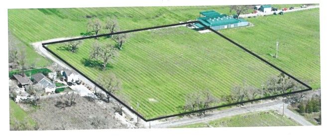 Aerial view of a rectangular field with a green crop, outlined in black, with structures and roads in the surroundings.